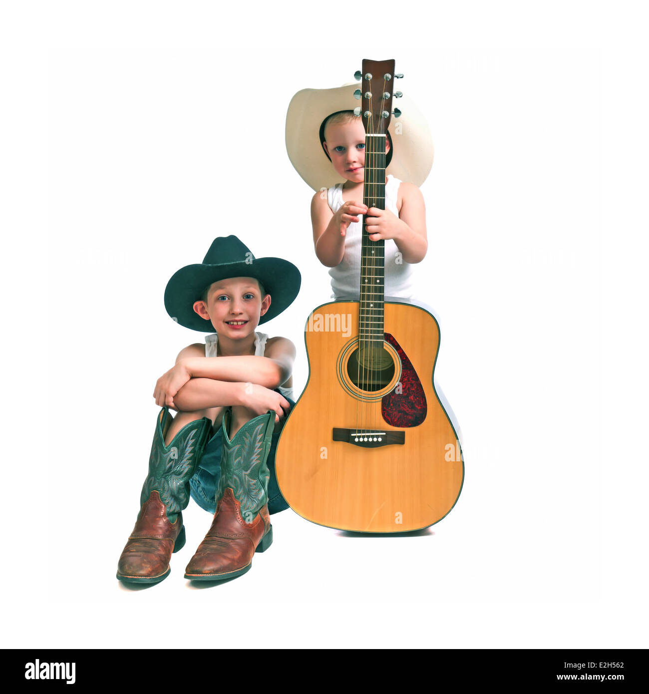 Pré-adolescents et un enfant d'âge préscolaire avec chapeaux de cow-boy , bottes et une guitare, isolé sur un fond blanc. Banque D'Images