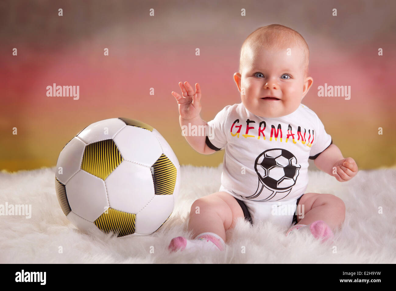 Baby girl, 7 mois, portant un maillot de football de l'Allemagne avec un ballon de football, l'allemand à l'arrière couleurs Banque D'Images