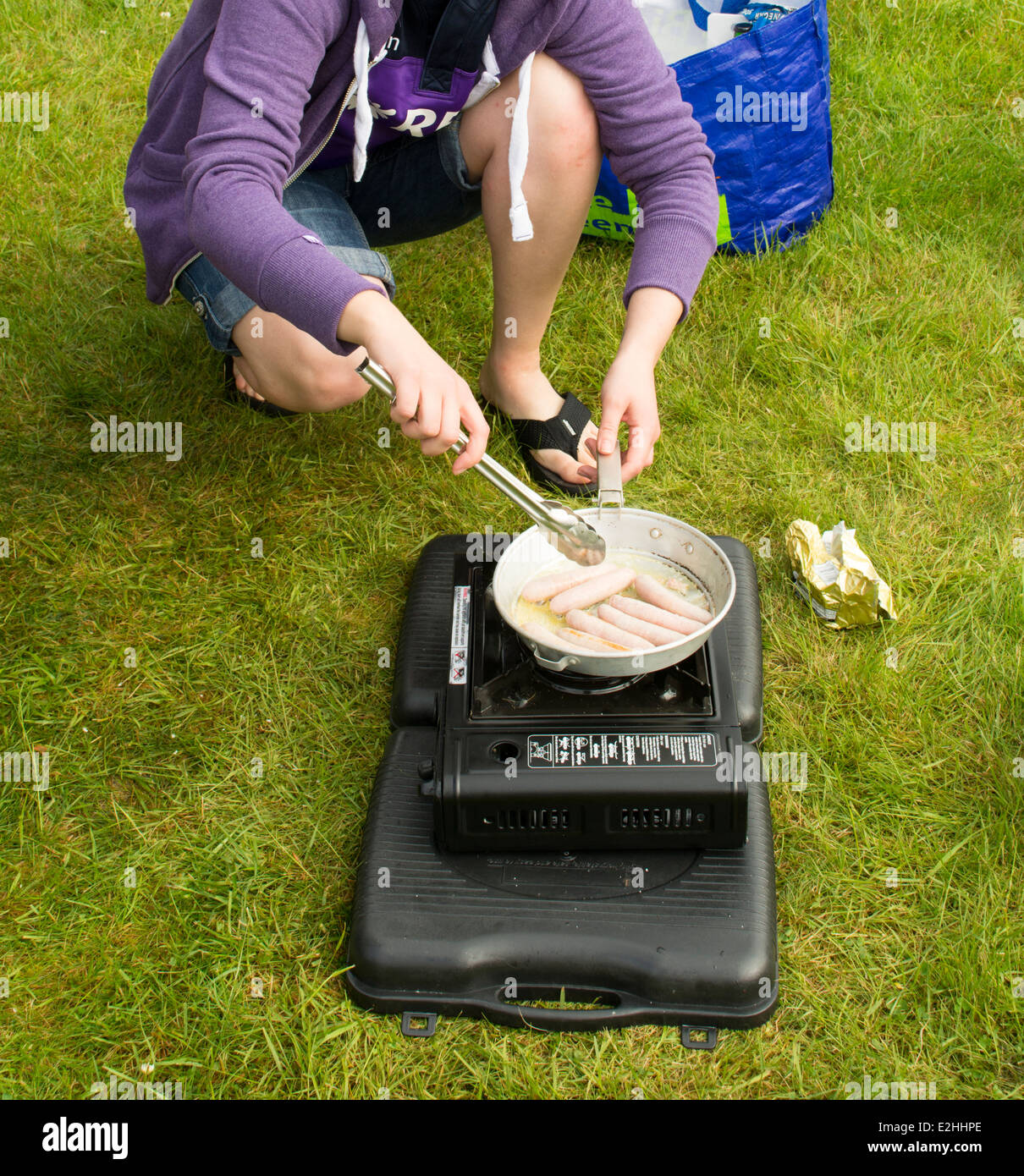 Une jeune femme en tongs saucisses cuisiniers pour le petit-déjeuner sur un réchaud  de camping Photo Stock - Alamy