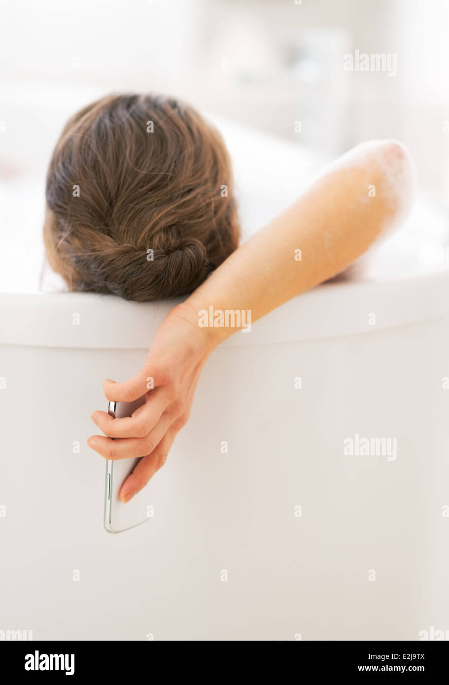 Young woman with cell phone pose en baignoire. Vue arrière Banque D'Images