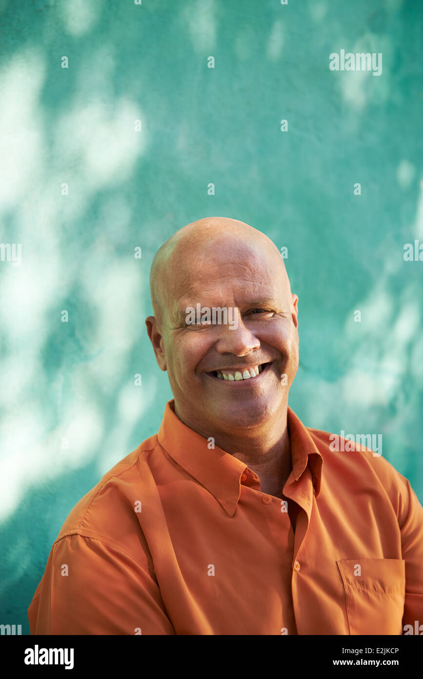Portrait of mature man avec orange shirt assis dans un parc et à la recherche à l'appareil photo avec l'expression heureuse Banque D'Images