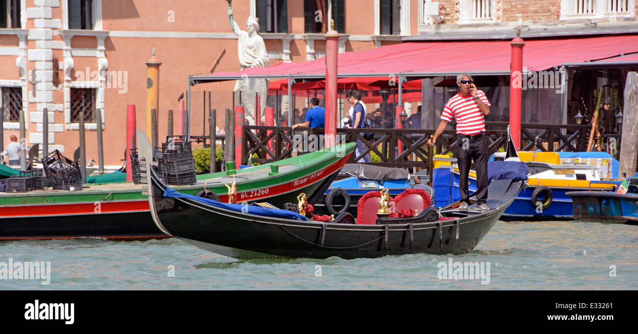 Vue rapprochée gondolier vénitien homme travaillant et debout un téléphone portable à bord de sa gondole à la station de la Grand Canal Venise Vénétie Italie Banque D'Images