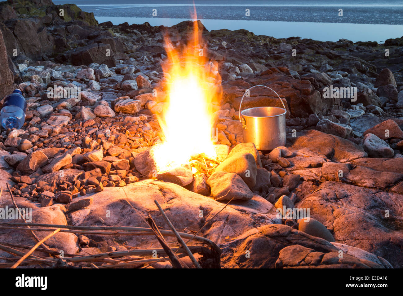Feu de camp avec casserole sur une plage de rochers au crépuscule England UK Banque D'Images