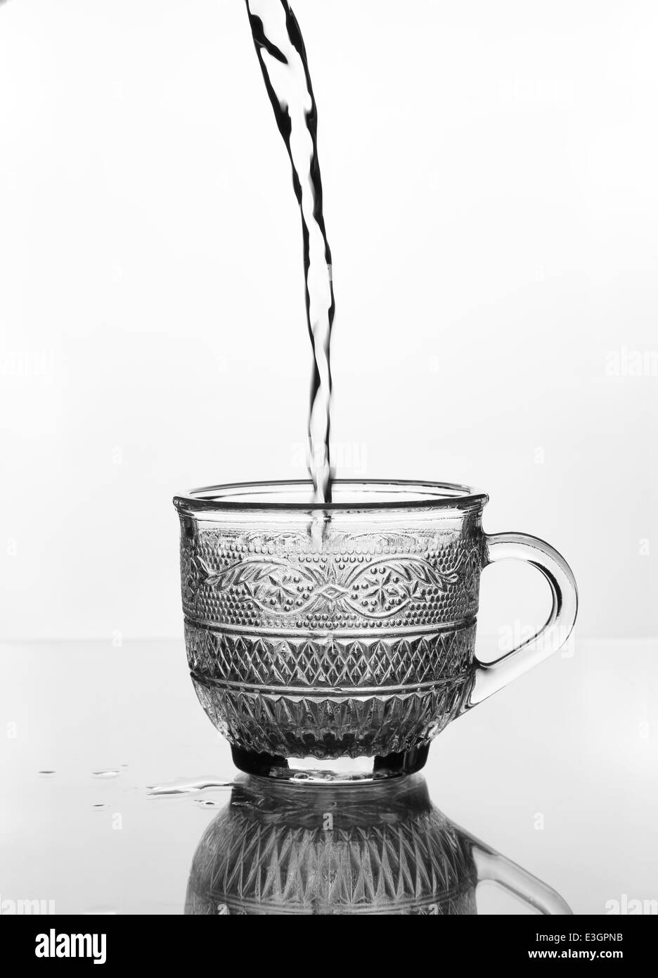 Verre tasse avec de l'eau verser sur une table en verre (échelle de gris) Banque D'Images