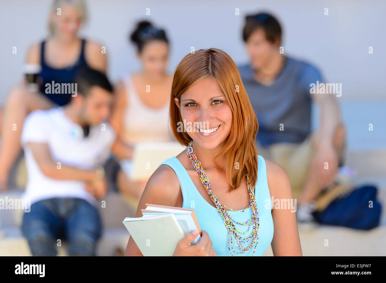Summer college student girl smiling holding books friends in background Banque D'Images