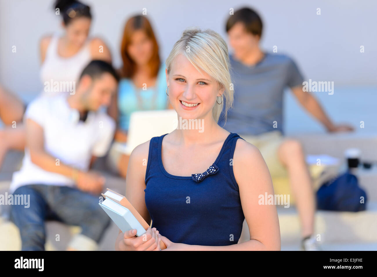 Teenage student girl smiling holding books amis en arrière-plan de l'été Banque D'Images