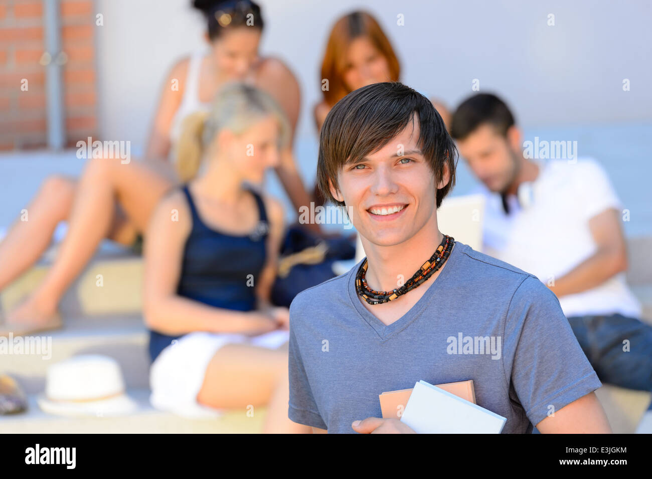 Smiling student garçon avec des amis à l'extérieur d'été collège holding books Banque D'Images