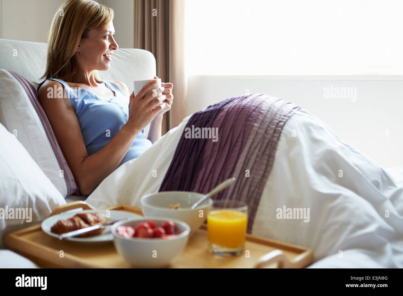 Détente d'âge moyen au lit avec boisson chaude et le petit déjeuner Banque D'Images