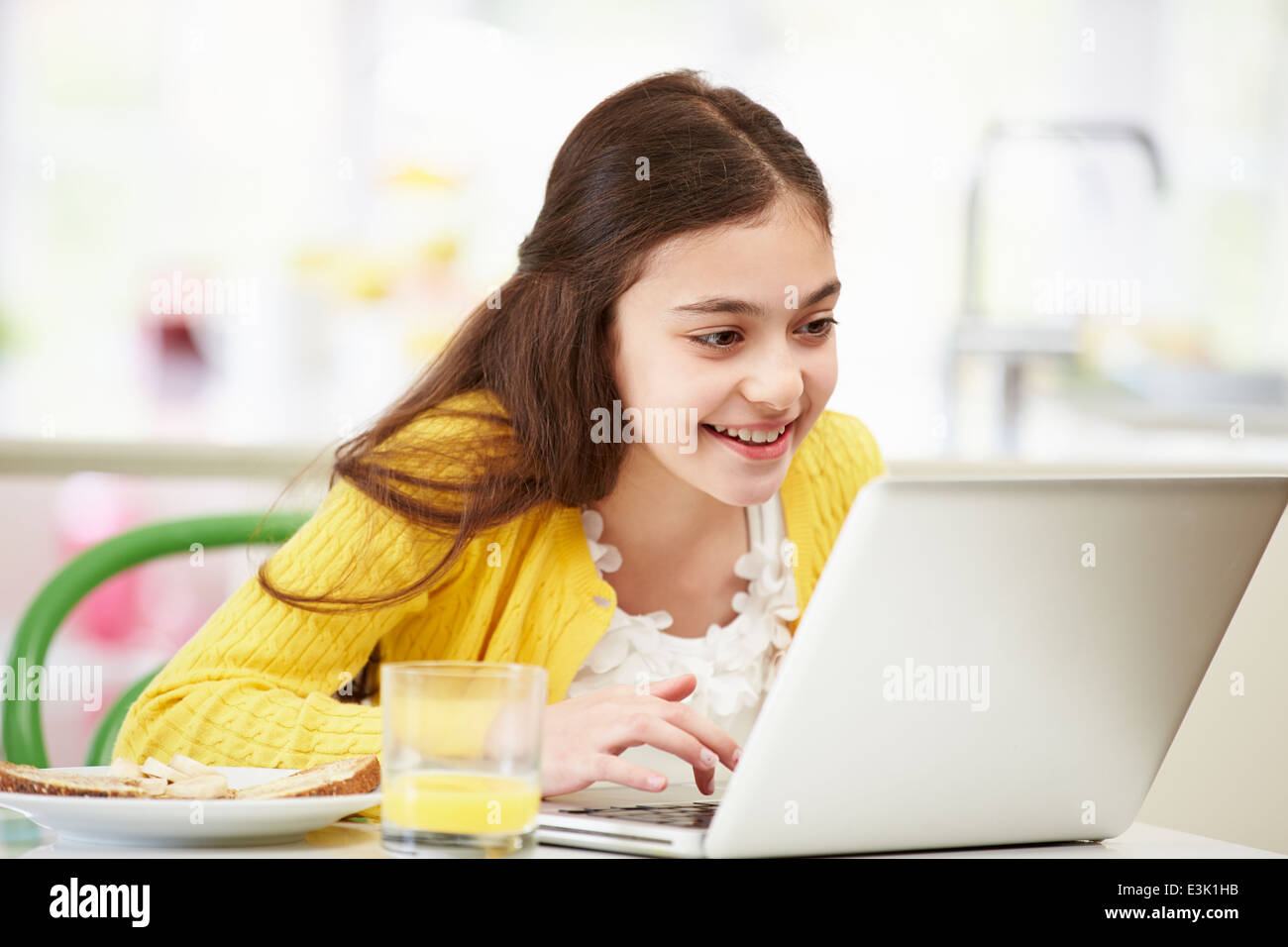 Hispanic Girl Using Laptop Eating Breakfast Banque D'Images
