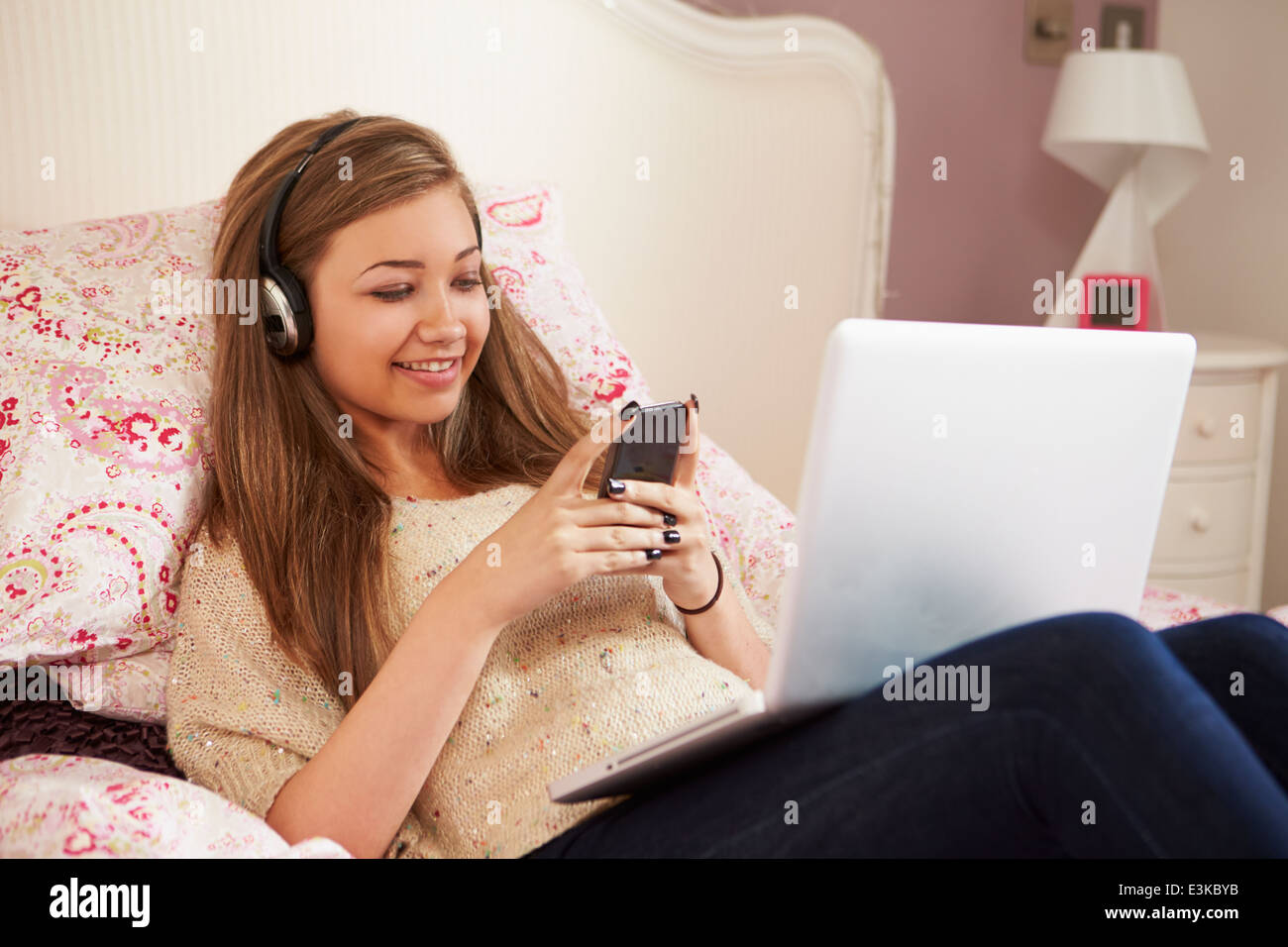 Teenage Girl Lying On Bed Using Laptop tout en Texting Banque D'Images