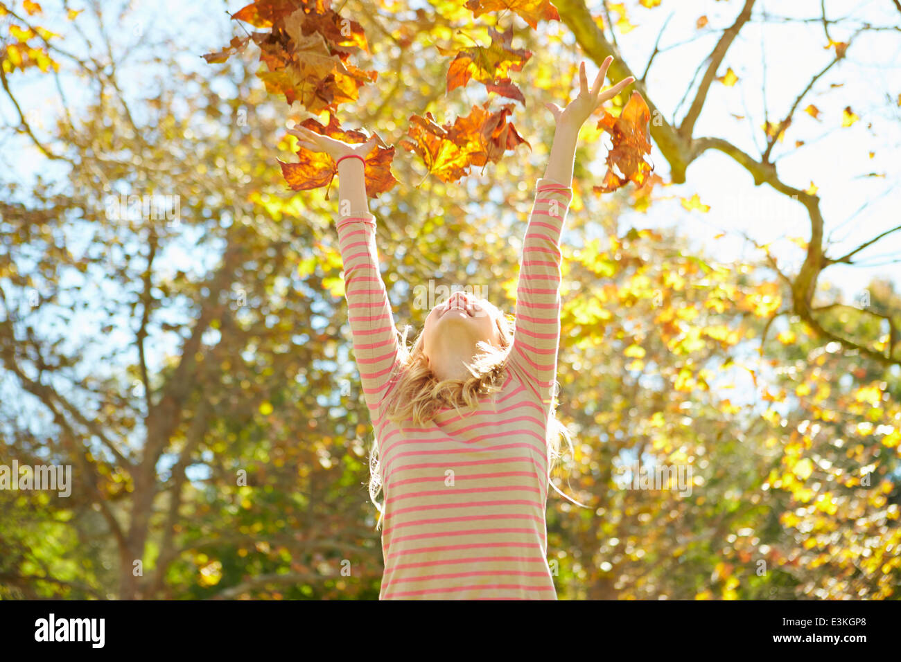 Jeune Fille de jeter les feuilles d'automne dans l'air Banque D'Images