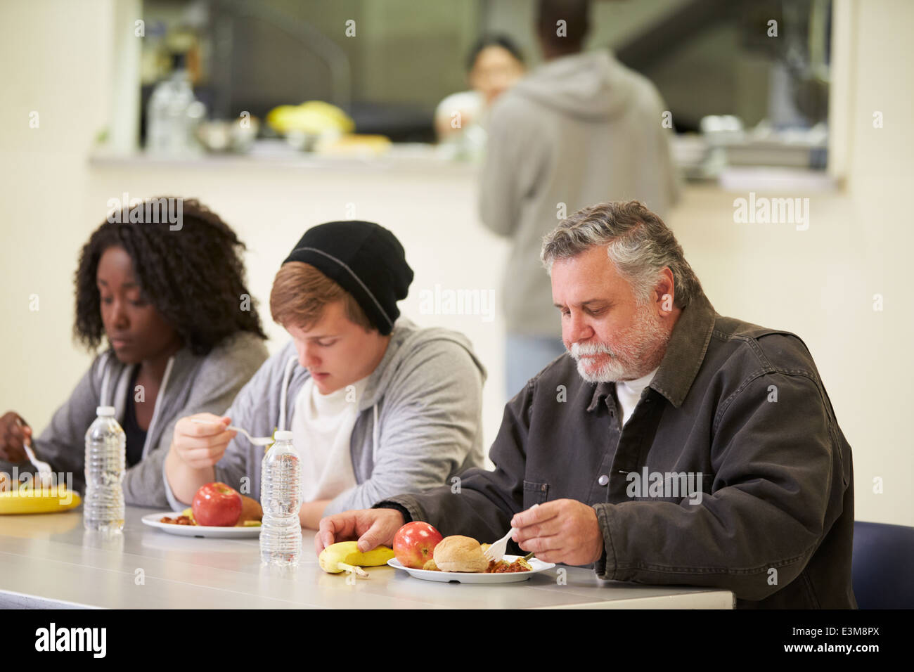 Les gens assis à table en train de manger la nourriture dans les sans-abris Banque D'Images