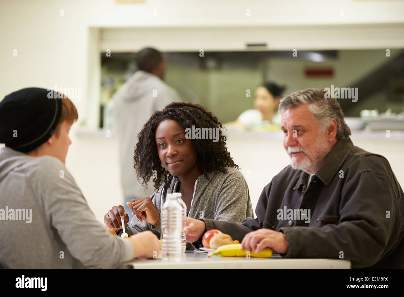 Les gens assis à table en train de manger la nourriture dans les sans-abris Banque D'Images