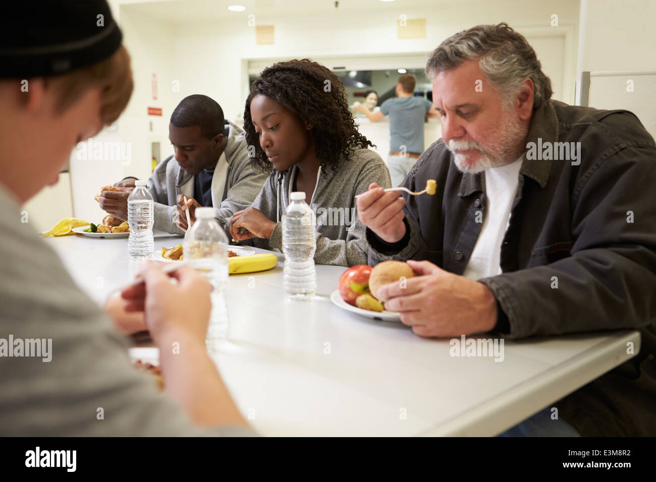 Les gens assis à table en train de manger la nourriture dans les sans-abris Banque D'Images