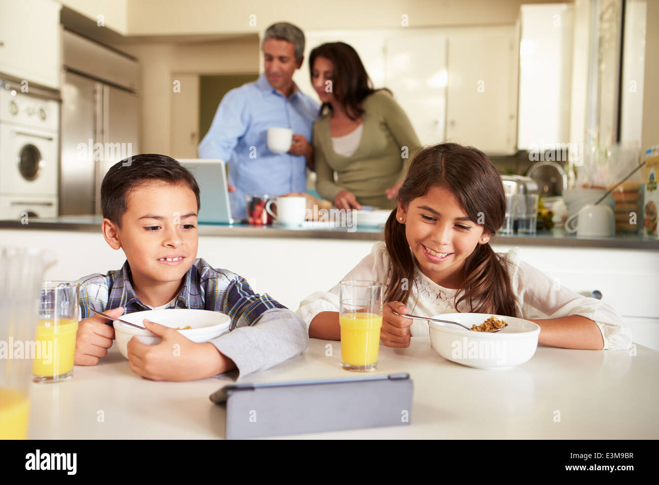 Hispanic Family Eating Breakfast en utilisant des appareils numériques Banque D'Images