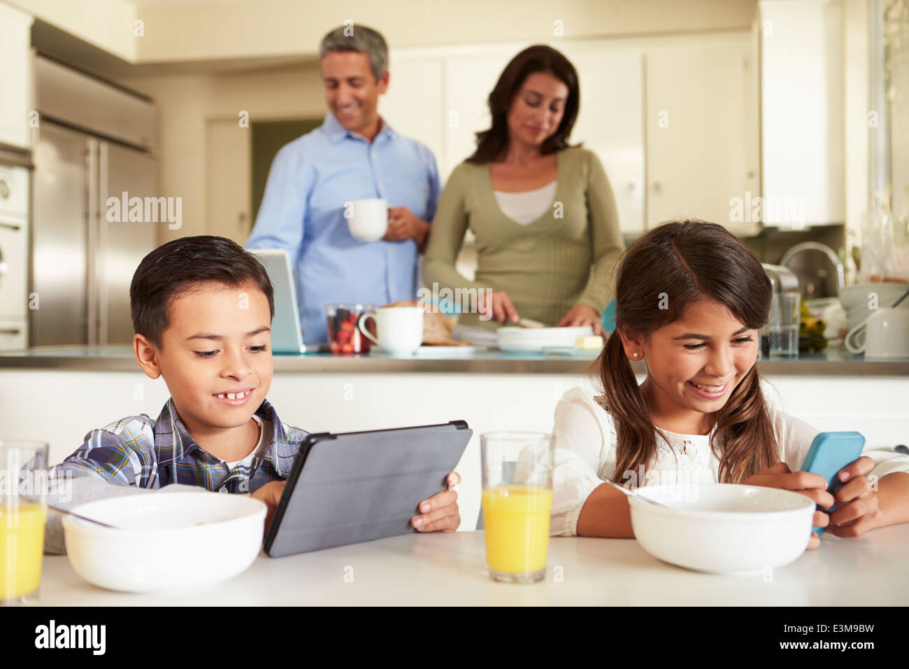 Hispanic Family Eating Breakfast en utilisant des appareils numériques Banque D'Images