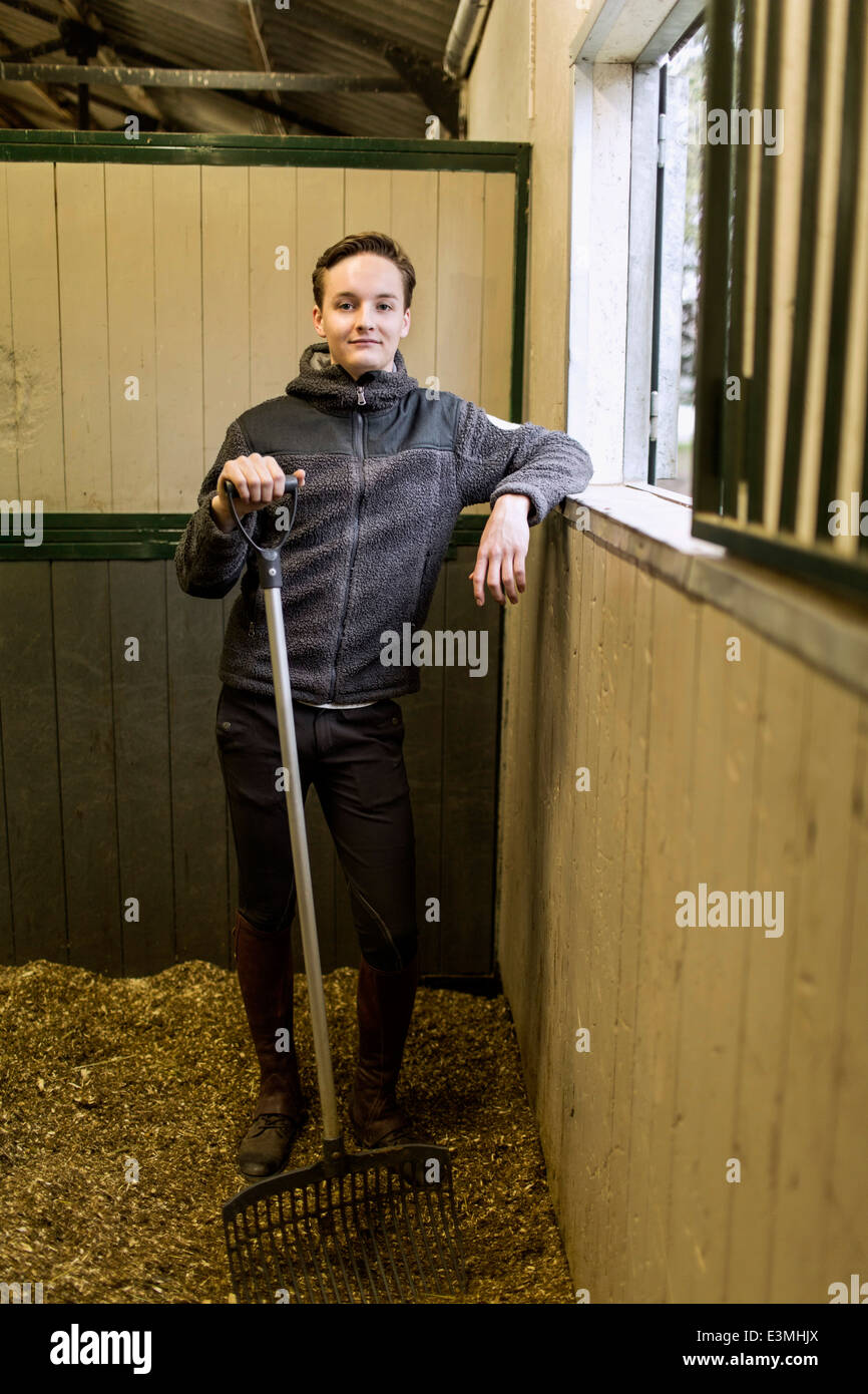 Portrait de jeune homme confiant et fourche dans horse stable Banque D'Images