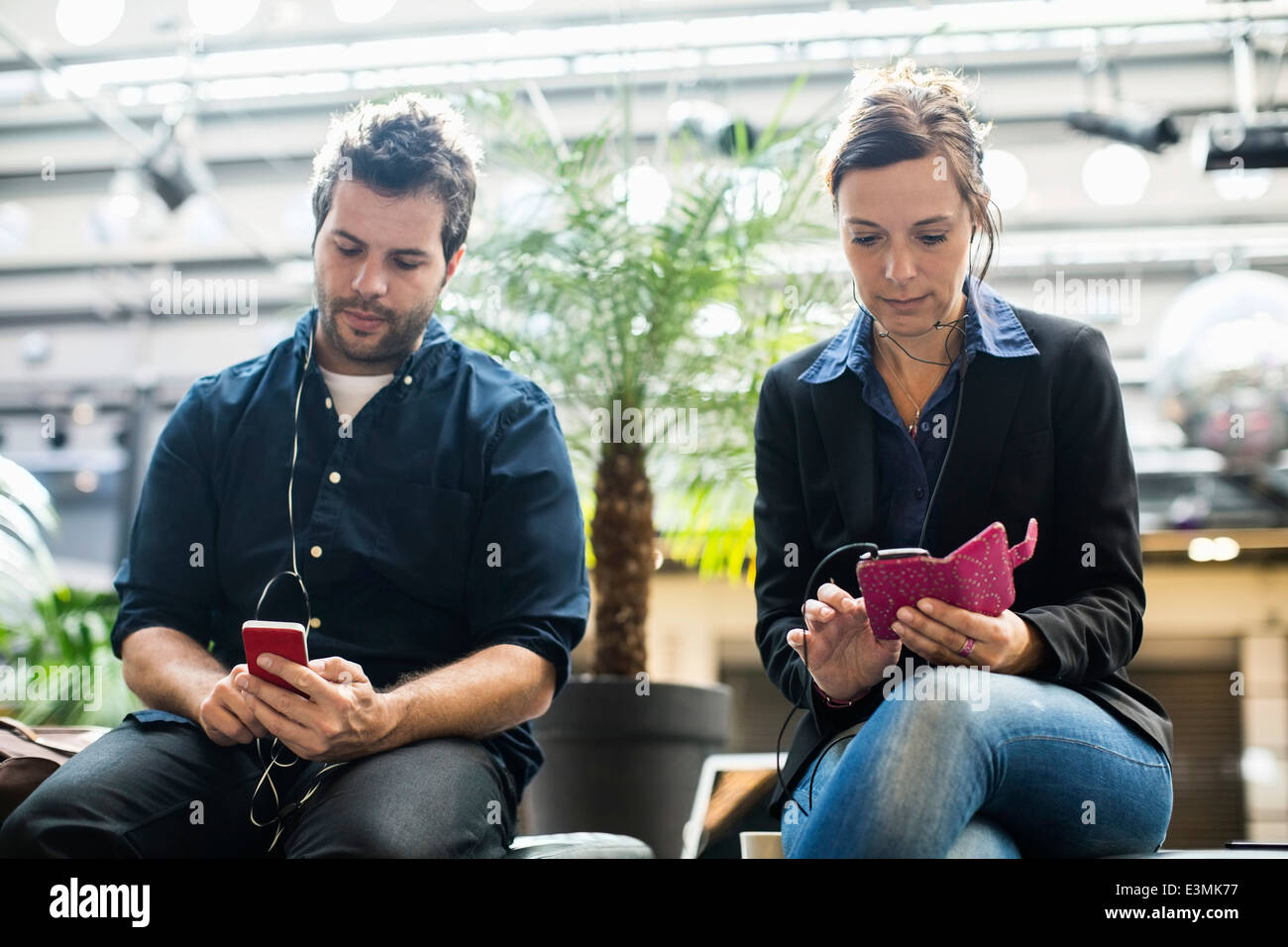 Businessman and businesswoman listening music sur téléphones mobiles dans cafe Banque D'Images