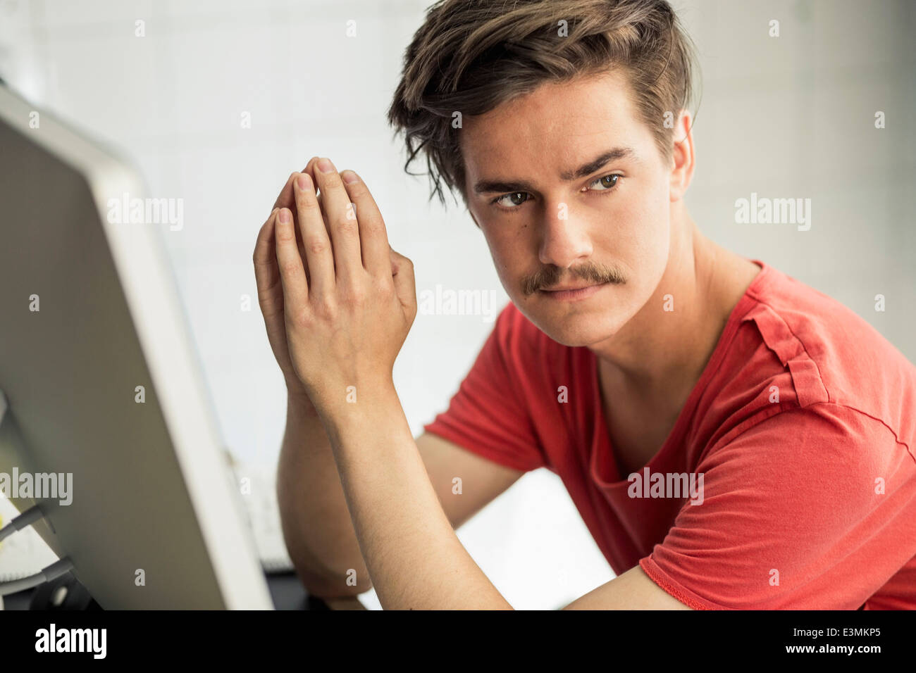 Young businessman with hands clasped sitting at computer desk in nouveau bureau Banque D'Images