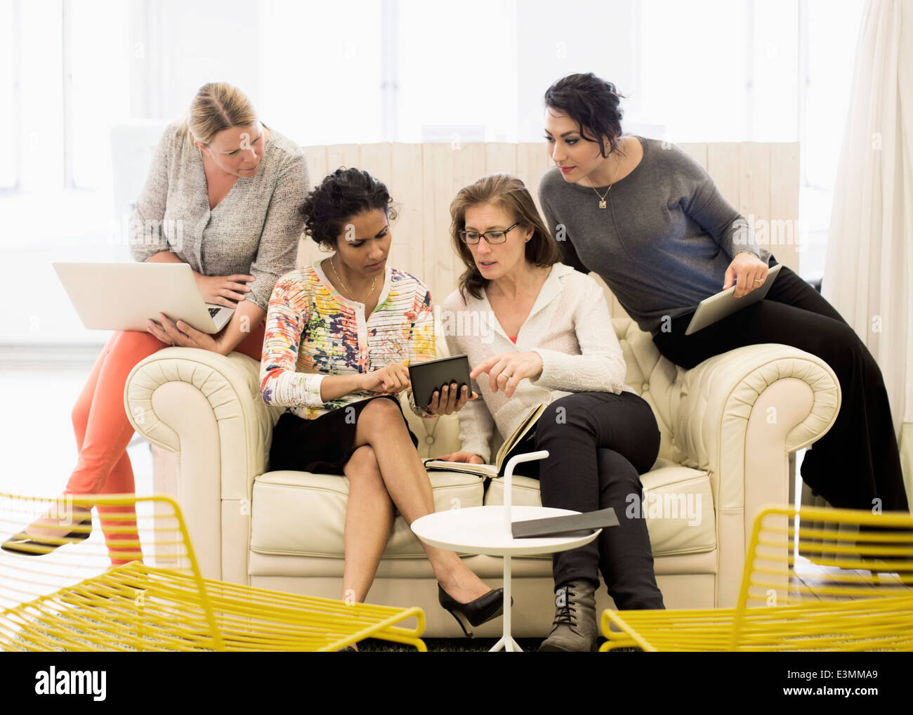 Creative businesswomen using digital tablet together on sofa in office Banque D'Images