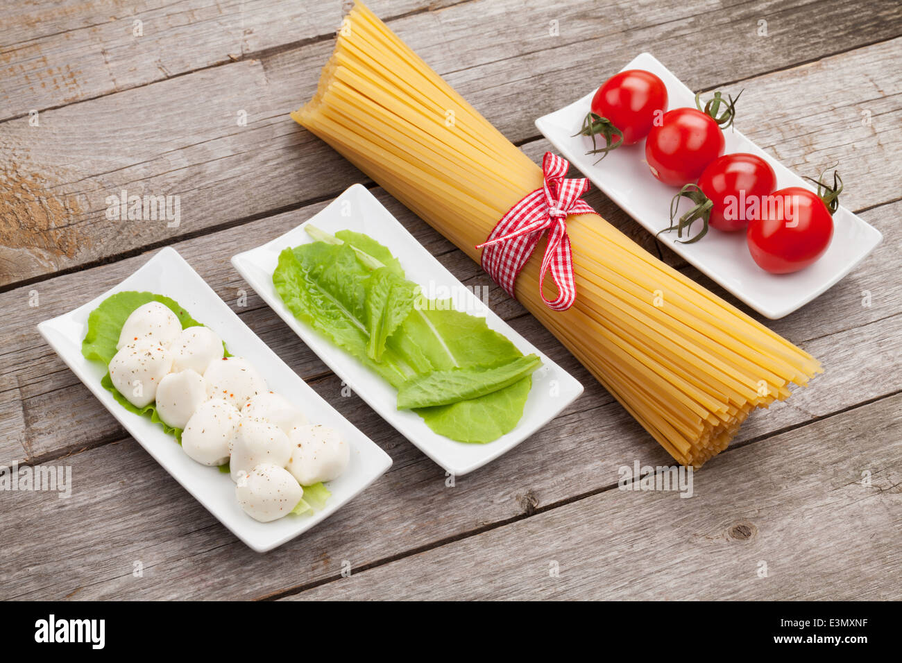 Tomates, mozzarella, pâtes et salade verte feuilles sur fond de table en bois Banque D'Images