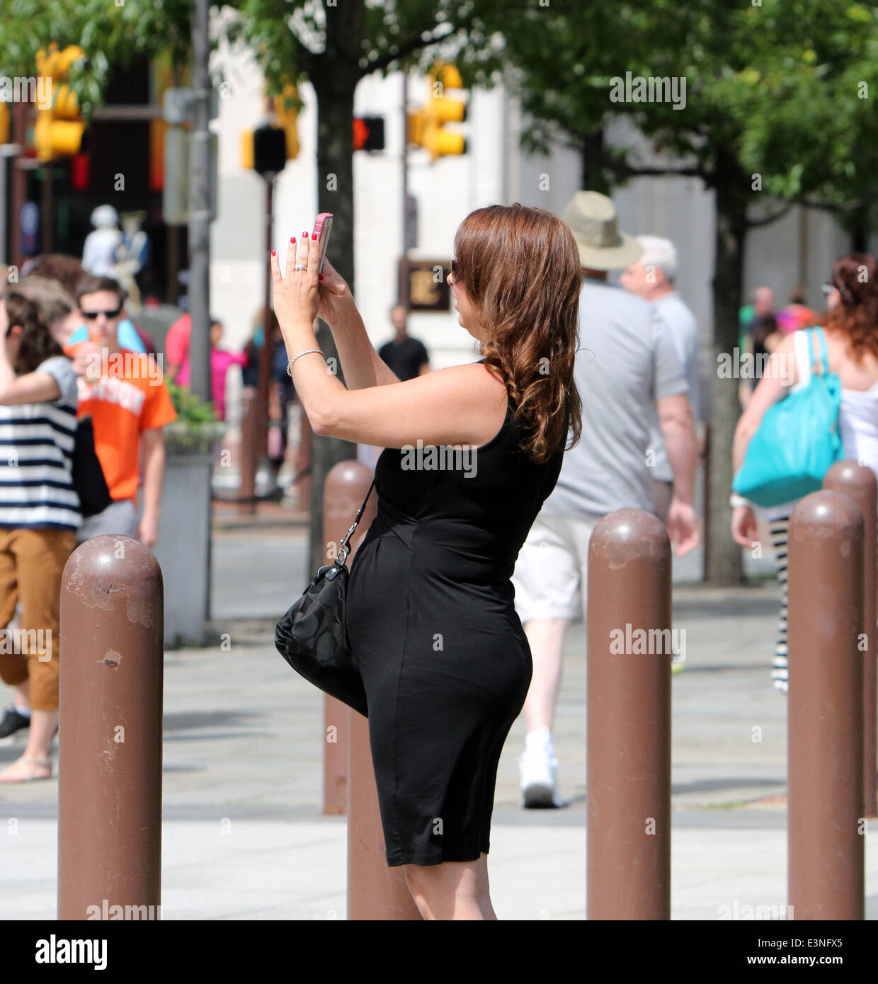 Femme enceinte dans une robe noire de prendre une photo avec son portable sur une rue de la ville. Banque D'Images