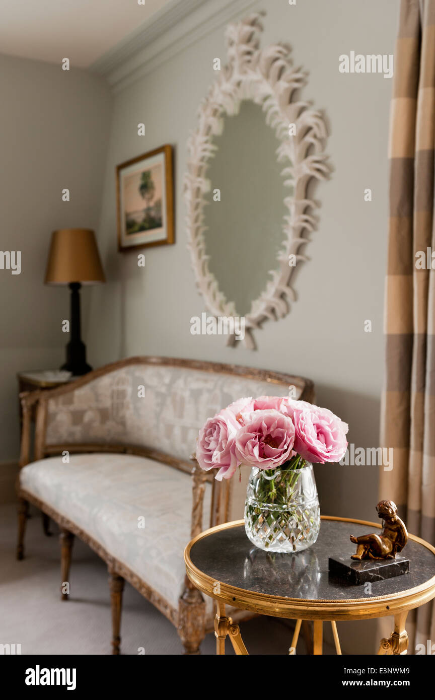 Roses en vase en verre sur la table ronde. Dans l'arrière-plan est un canapé antique sous un miroir encadré de plâtre Banque D'Images