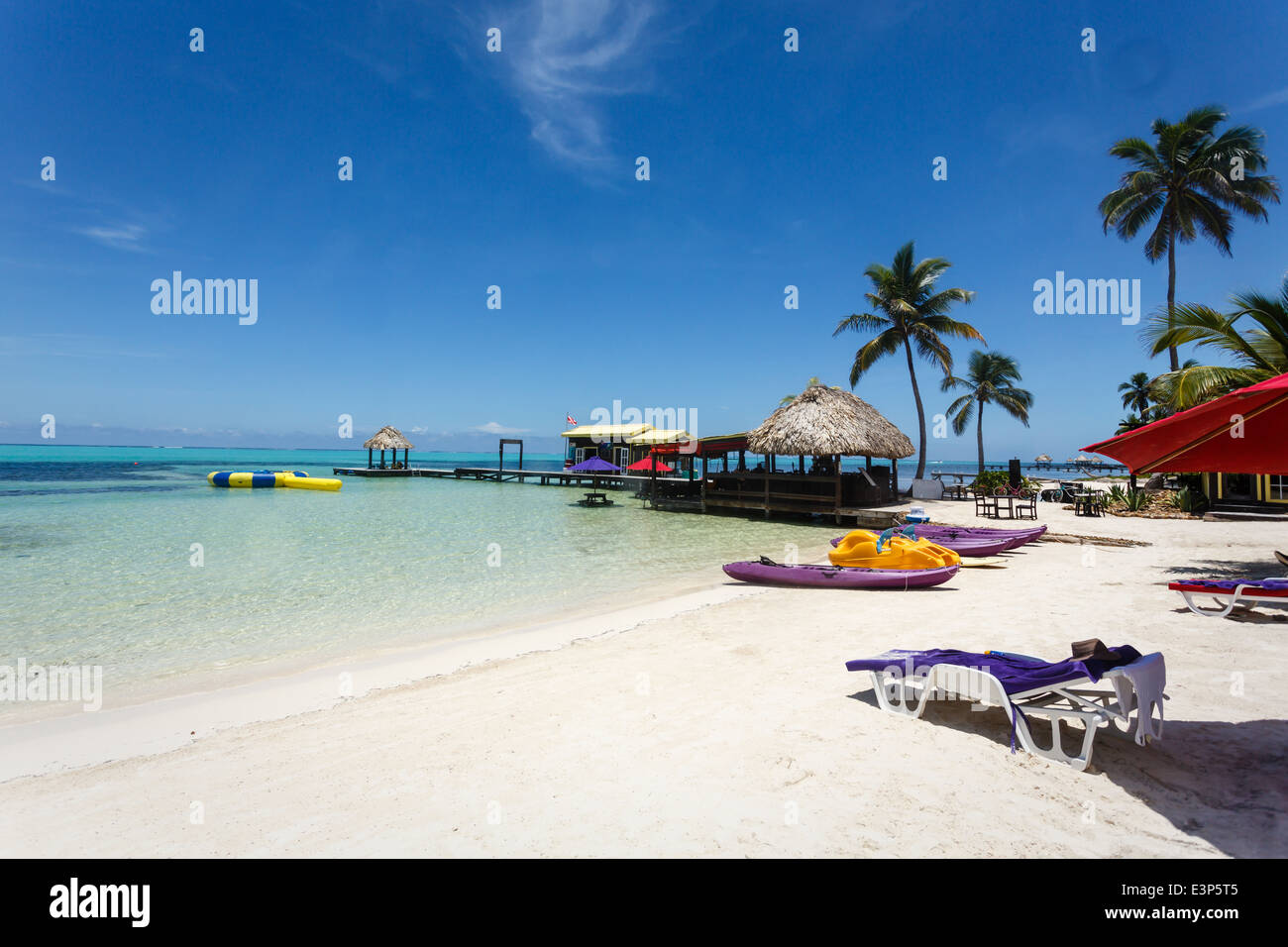 Paysage relaxant d'une station balnéaire avec du sable blanc, des cabanes tikki au toit de chaume et des palmiers. Banque D'Images