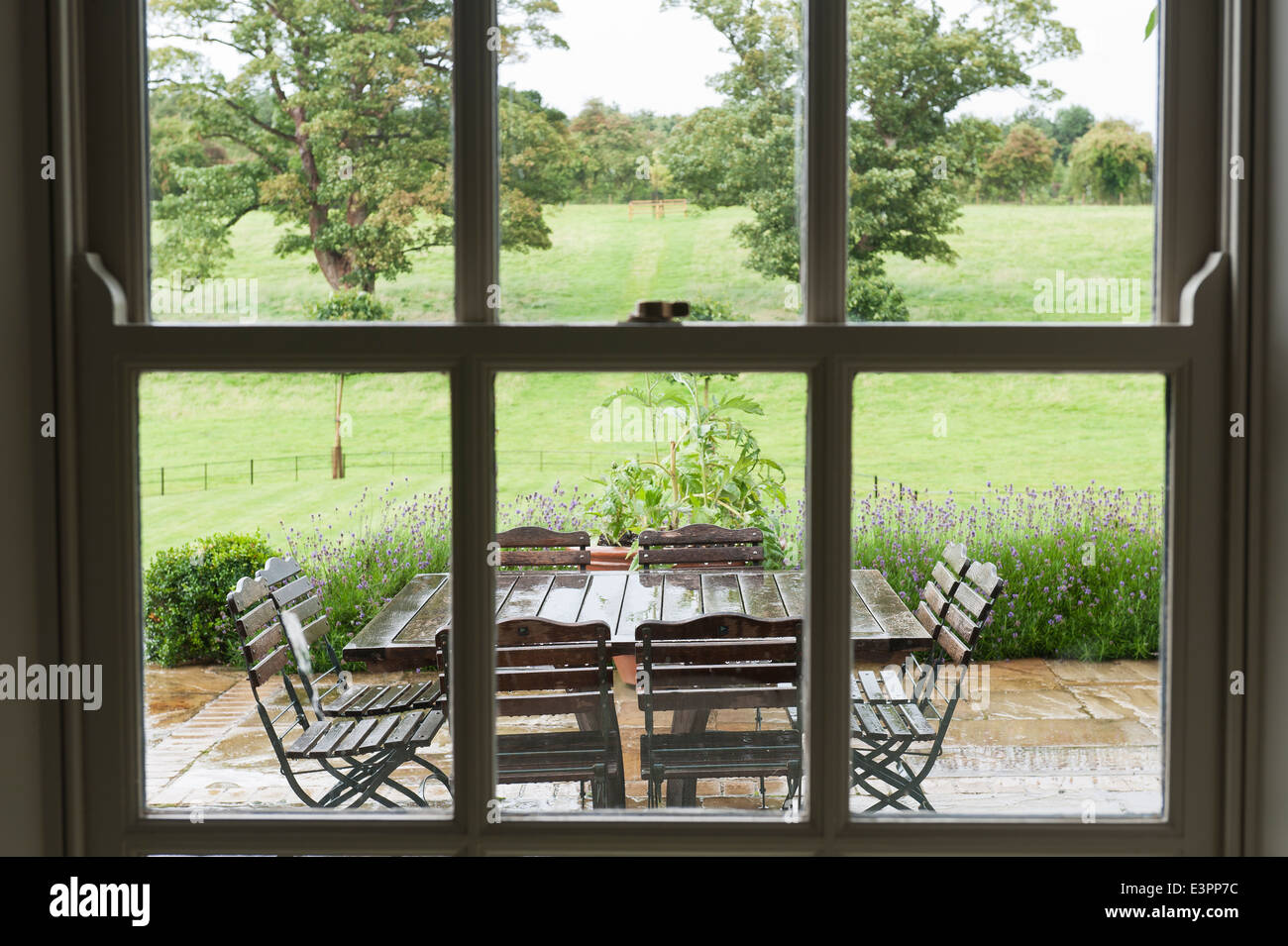 Vue à travers la fenêtre à vitrage jardin humide terrasse avec mobilier de jardin Banque D'Images