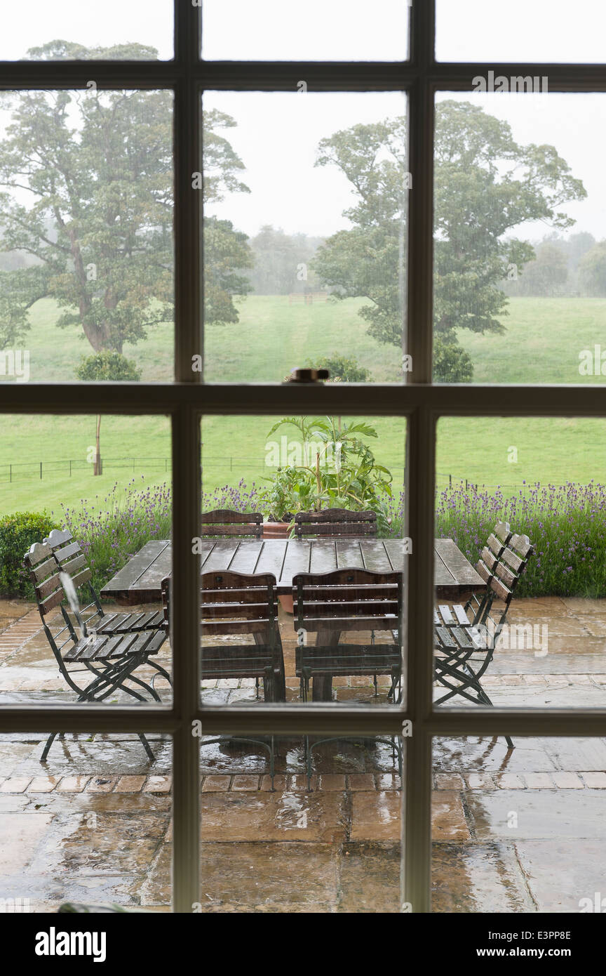 Vue à travers la fenêtre à vitrage jardin humide terrasse avec mobilier de jardin Banque D'Images