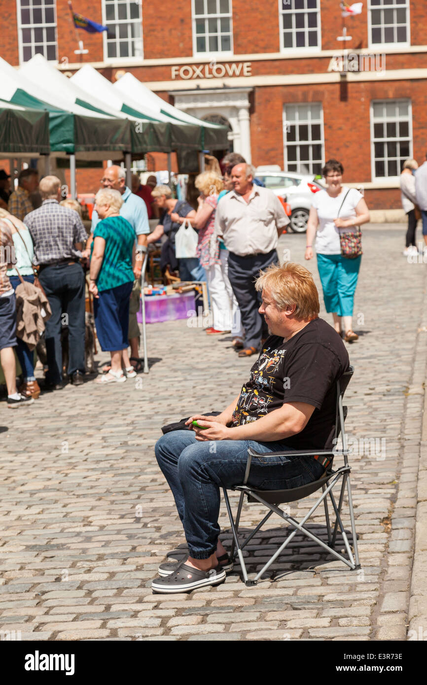 UK Angleterre , Poireau, Staffordshire, un jeune homme assis sur une chaise à côté de son stand, la messagerie texte sur téléphone mobile. Banque D'Images