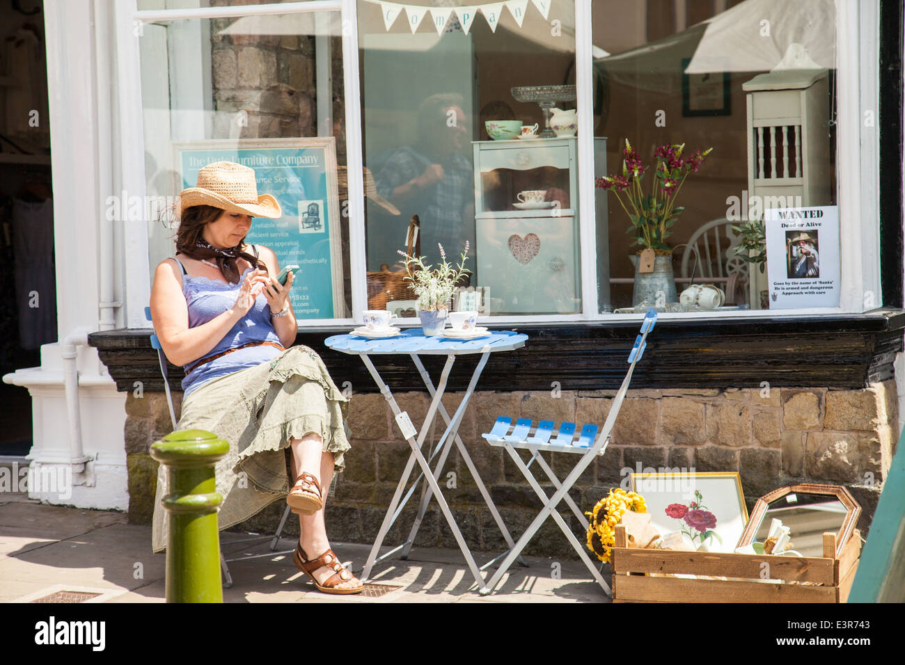 UK ,Angleterre Poireau, Staffordshire, une jeune femme assise sur une chaise à l'extérieur d'un magasin de meubles la messagerie texte sur un téléphone mobile, Banque D'Images