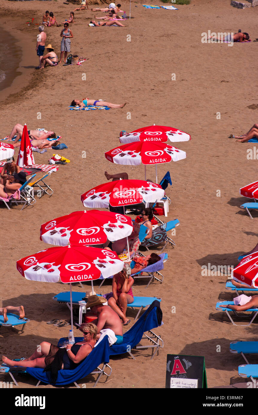 Les gens en train de bronzer sur une plage de sable sur les transats sous les parasols Banque D'Images