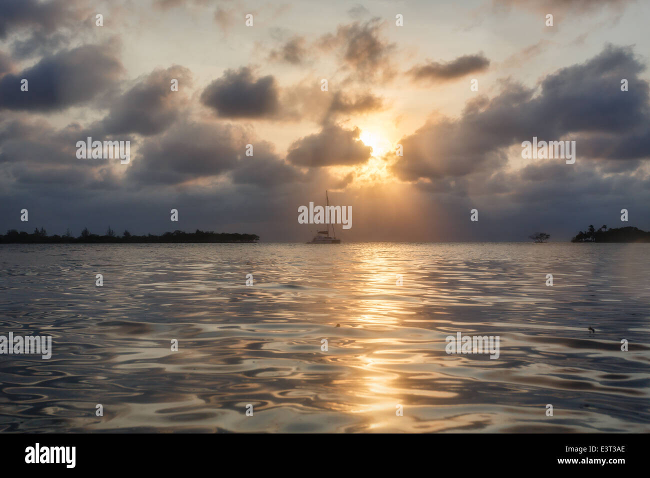 Voilier silhouetté contre le ciel orageux au coucher du soleil au large de la côte du Belize Banque D'Images