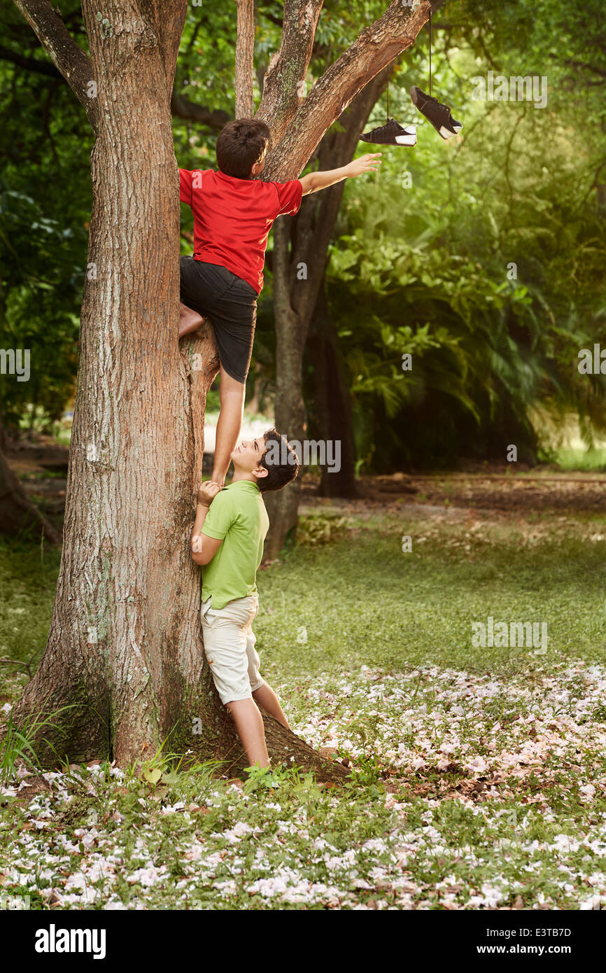 Deux enfants d'aider les uns les autres pour grimper sur un arbre et d'atteindre pour les chaussures on branch Banque D'Images