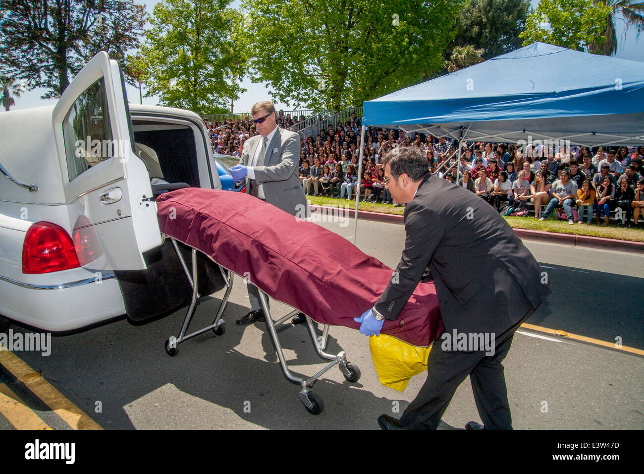 Des bénévoles locaux undertakers charger le 'Corpse' de la victime d'un accident dans un corbillard dans une dramatisation pour des élèves du secondaire sur les dangers de l'alcool au volant à Anaheim, CA. Remarque foule en arrière-plan. Banque D'Images