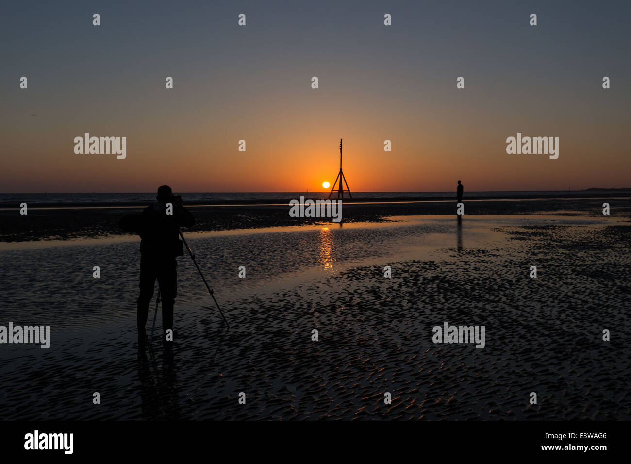 Un homme utilise une caméra et trépied pour photographier le solstice d'été à Crosby Beach de Sefton, nord-ouest de l'Angleterre. Banque D'Images