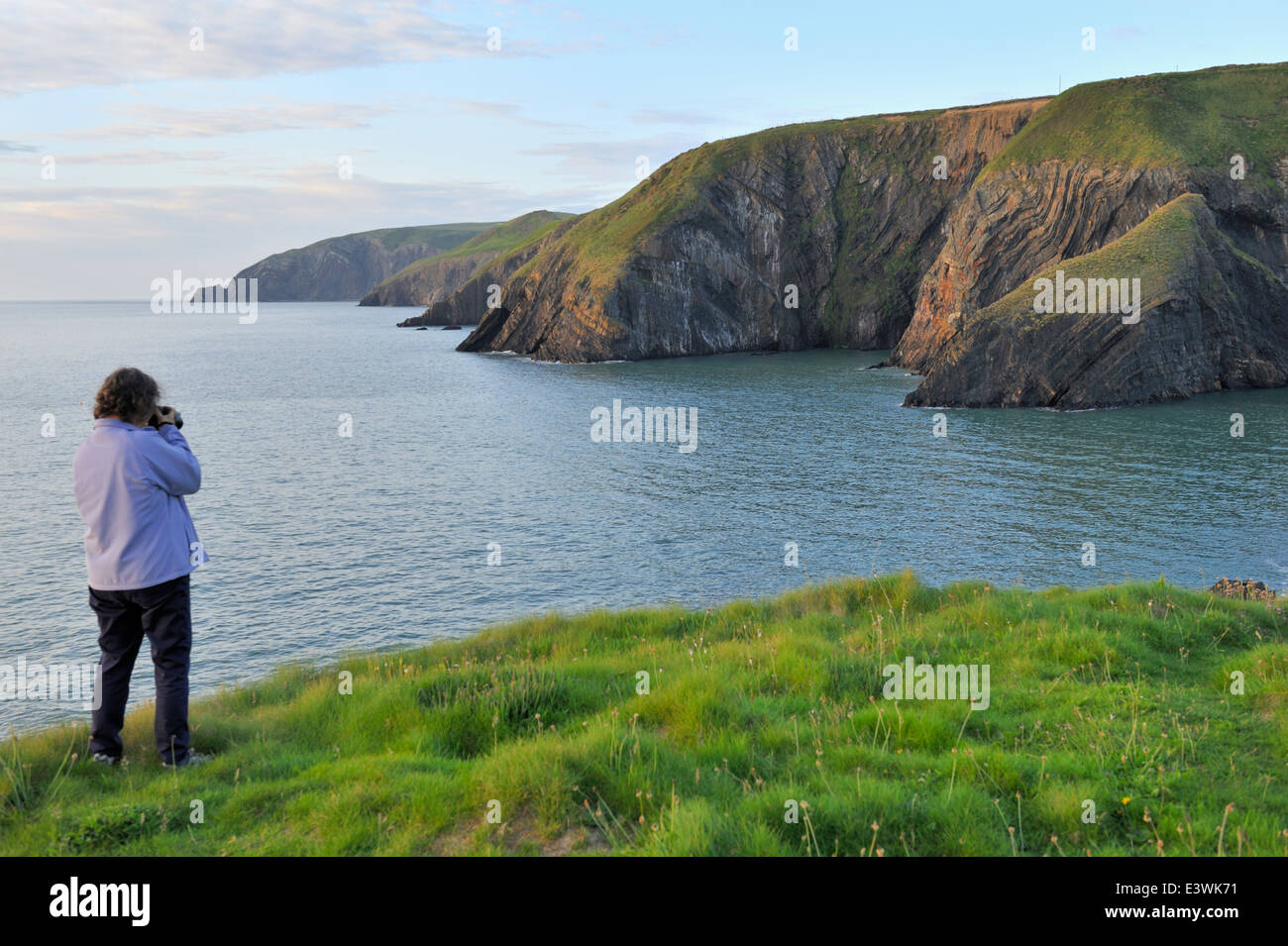 Début de soirée femme avec caméra sur champ vert le long de la côte du Pembrokeshire, Pays de Galles de l'ouest. Près de la Baie d'Ceibwr Banque D'Images
