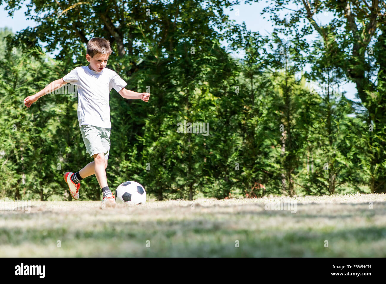 Enfant jouant au football dans un stade. Des arbres sur l'arrière-plan Banque D'Images