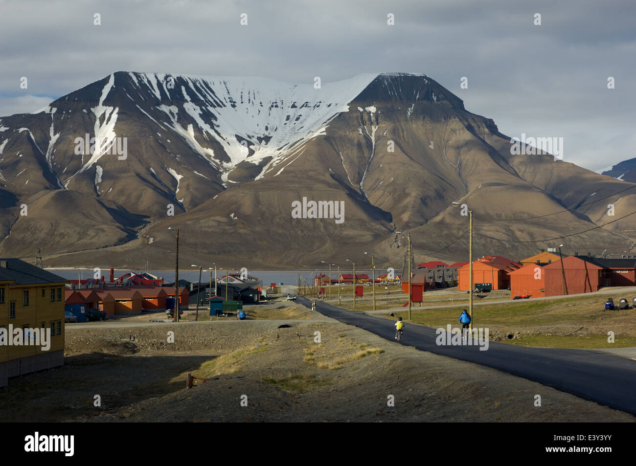 Randonnée à vélo le long de la rue principale à travers les logements aux couleurs vives et aux entreprises, avec la montagne en arrière-plan Hiorthfjellet, Longyearbyen, Spitzberg, archipel du Svalbard, Norvège Banque D'Images