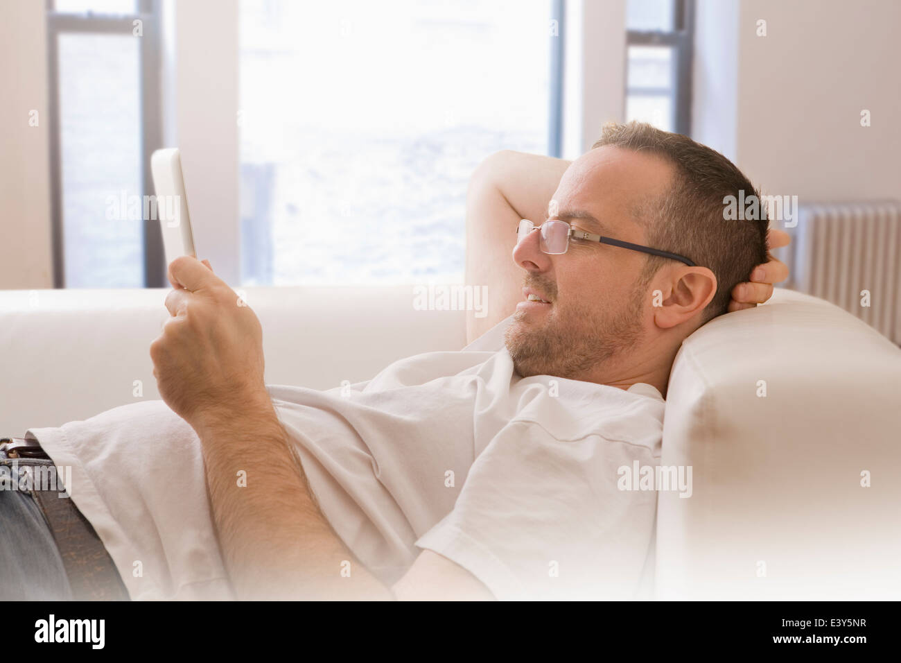 Man reclining on sofa looking at digital tablet Banque D'Images