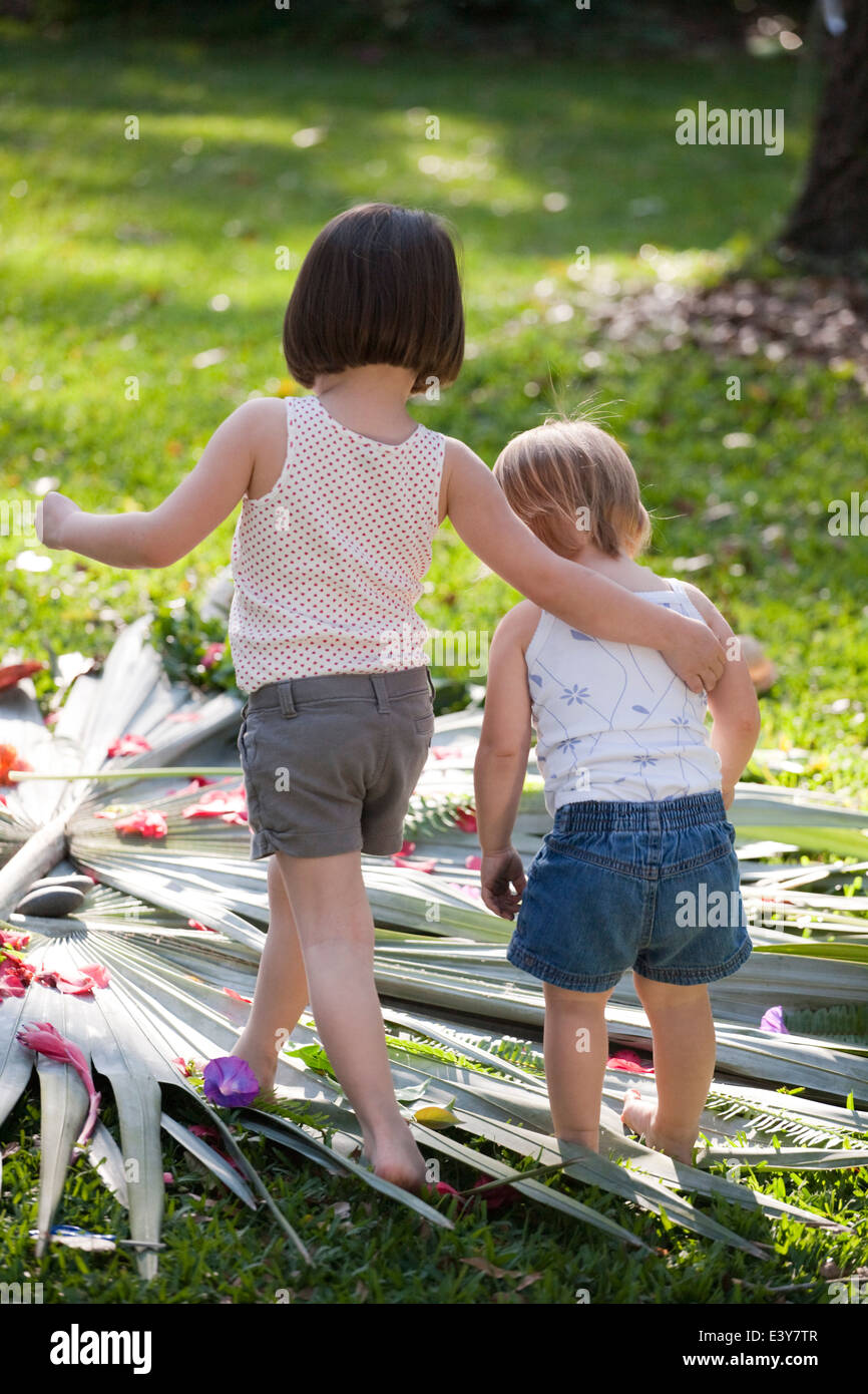 Fille avec bras autour de tout-petit soeur avec fleur et feuille afficher dans jardin Banque D'Images