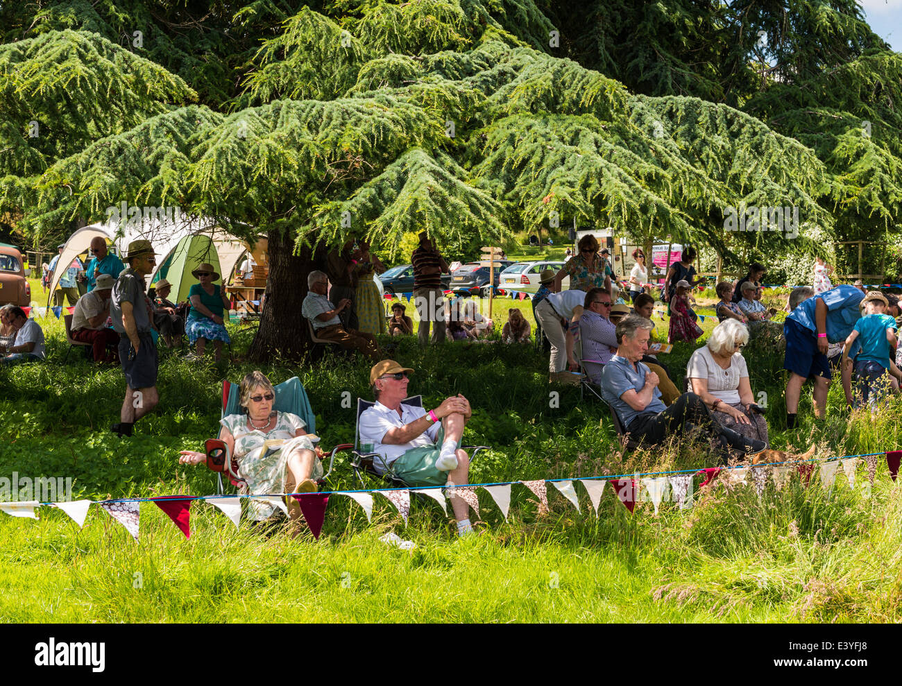 L'est du Devon, Angleterre. Les gens s'assoient à vous détendre sous l'ombre d'un grand arbre à la fete et garden party au cours de l'été. Banque D'Images
