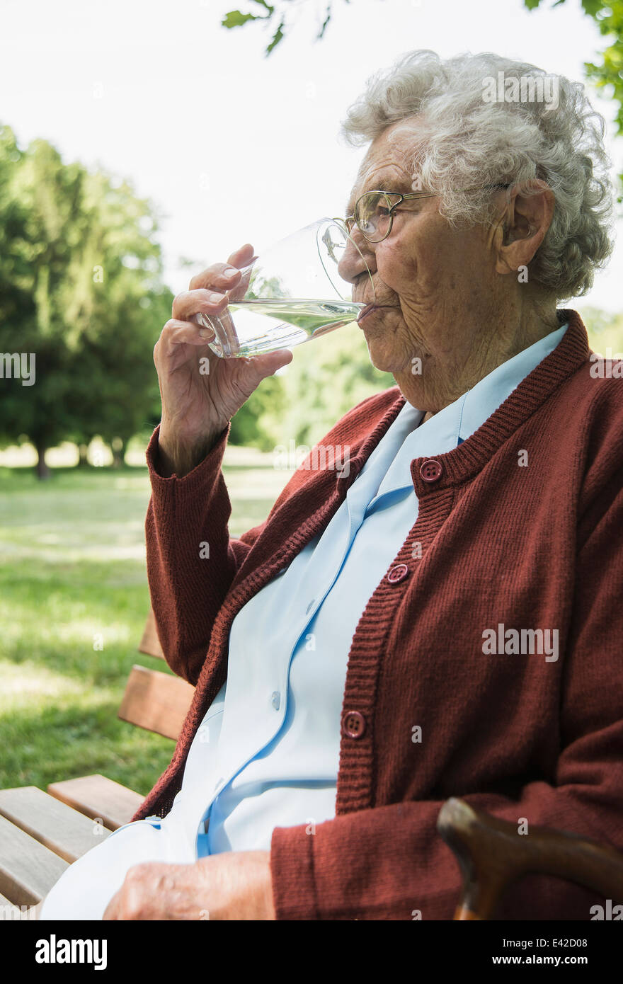 Senior woman sitting on park bench, verre d'eau potable Banque D'Images
