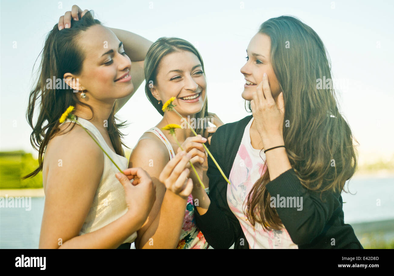 Trois jeunes amis féminins on riverbank holding pissenlits Banque D'Images