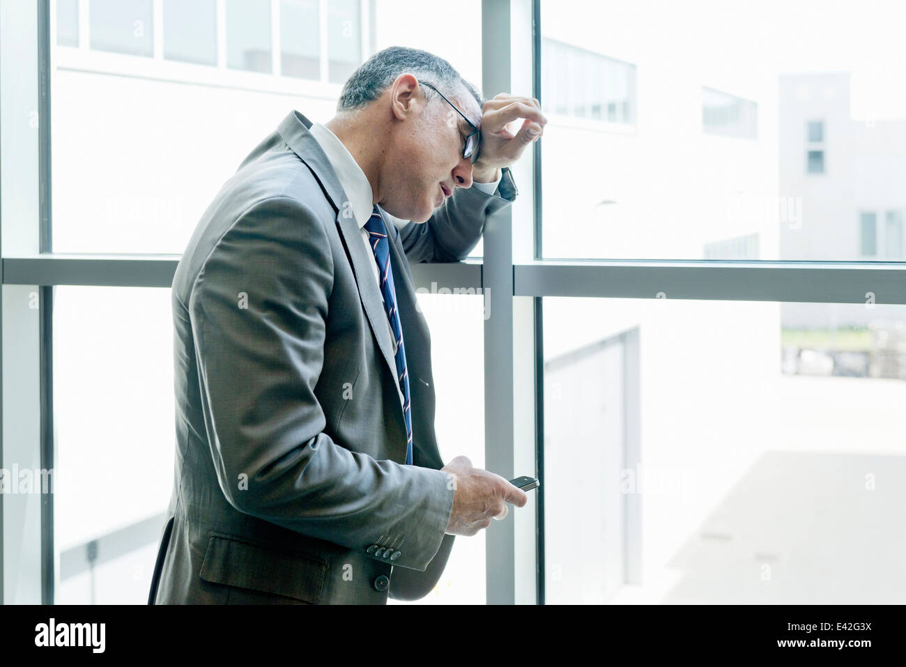 Businessman leaning on smartphone avec mur de verre Banque D'Images