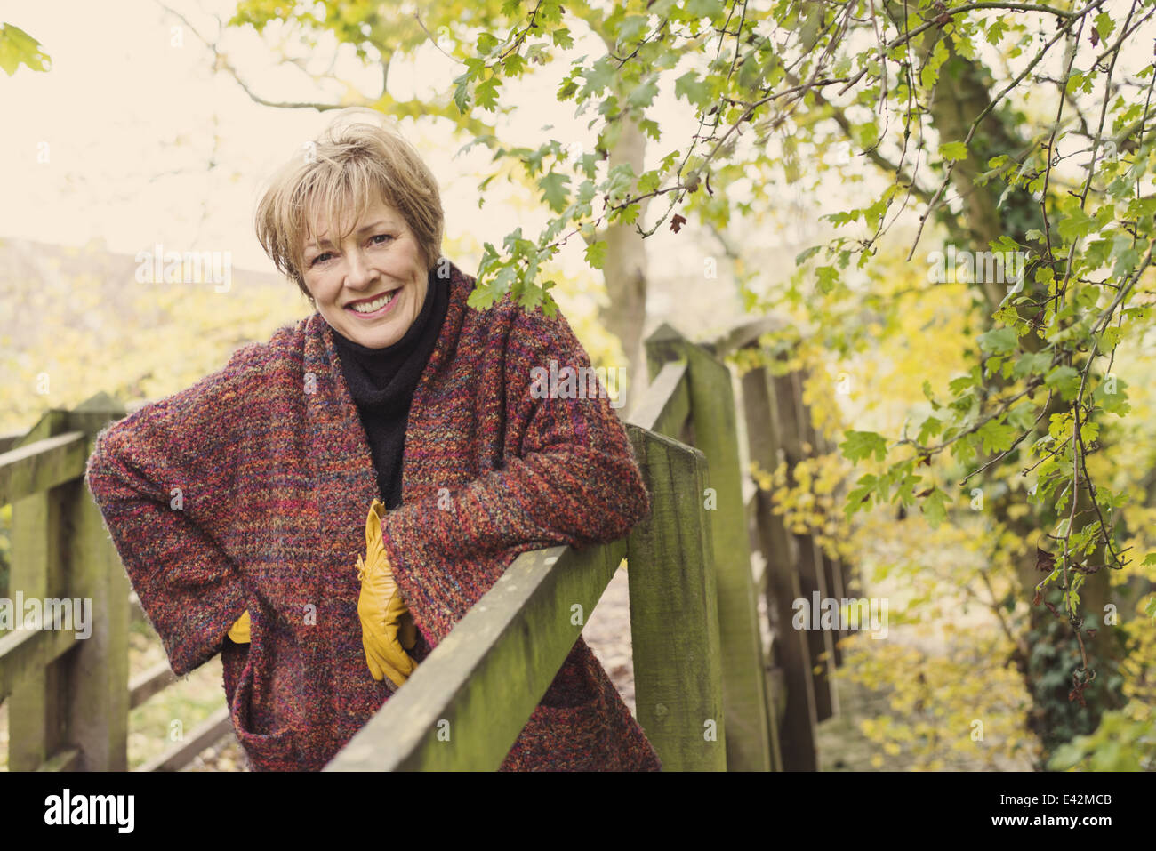 Mature Woman leaning on wooden fence, smiling Banque D'Images