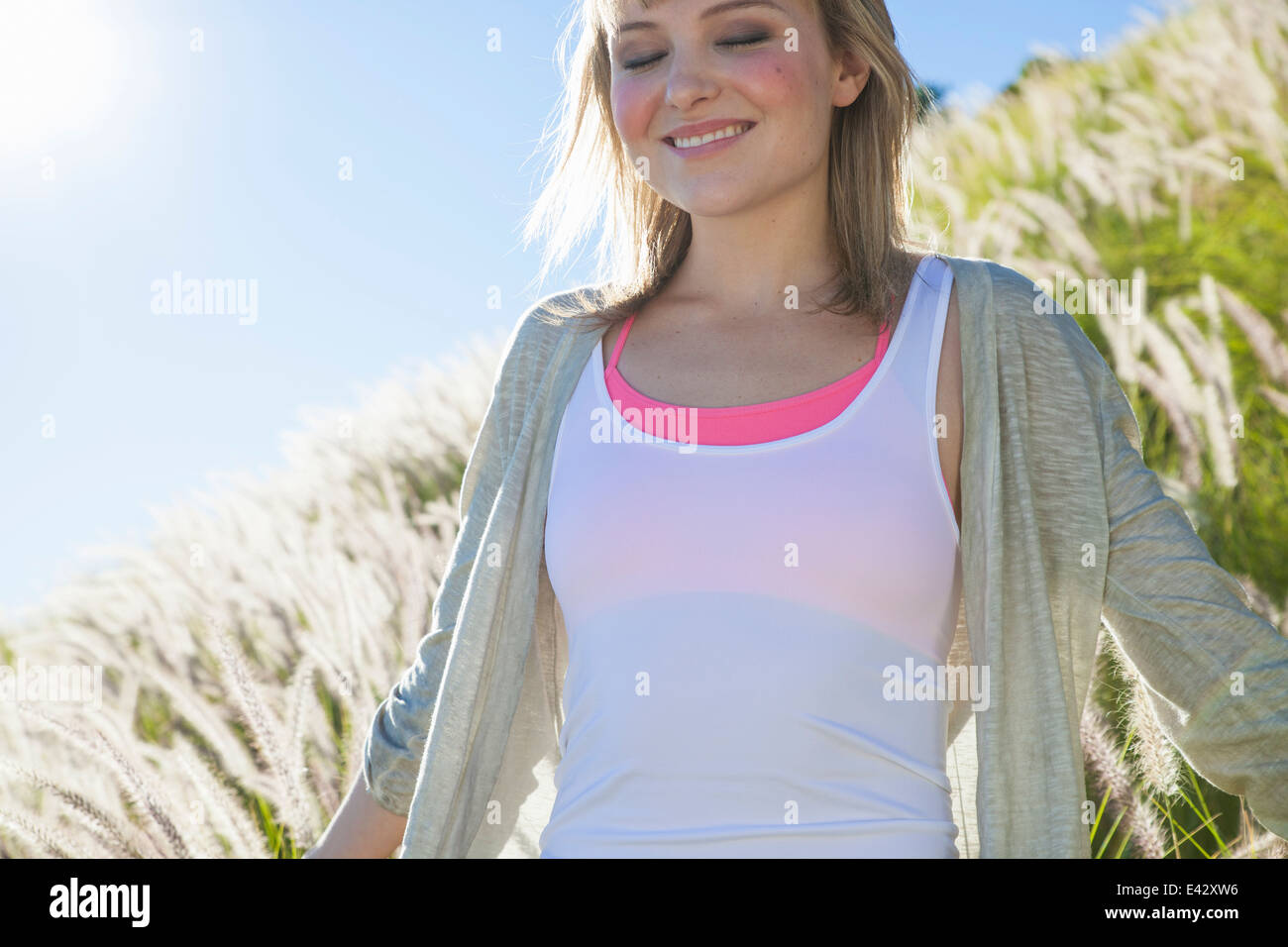Young woman smiling avec les yeux fermés dans l'herbe haute Banque D'Images