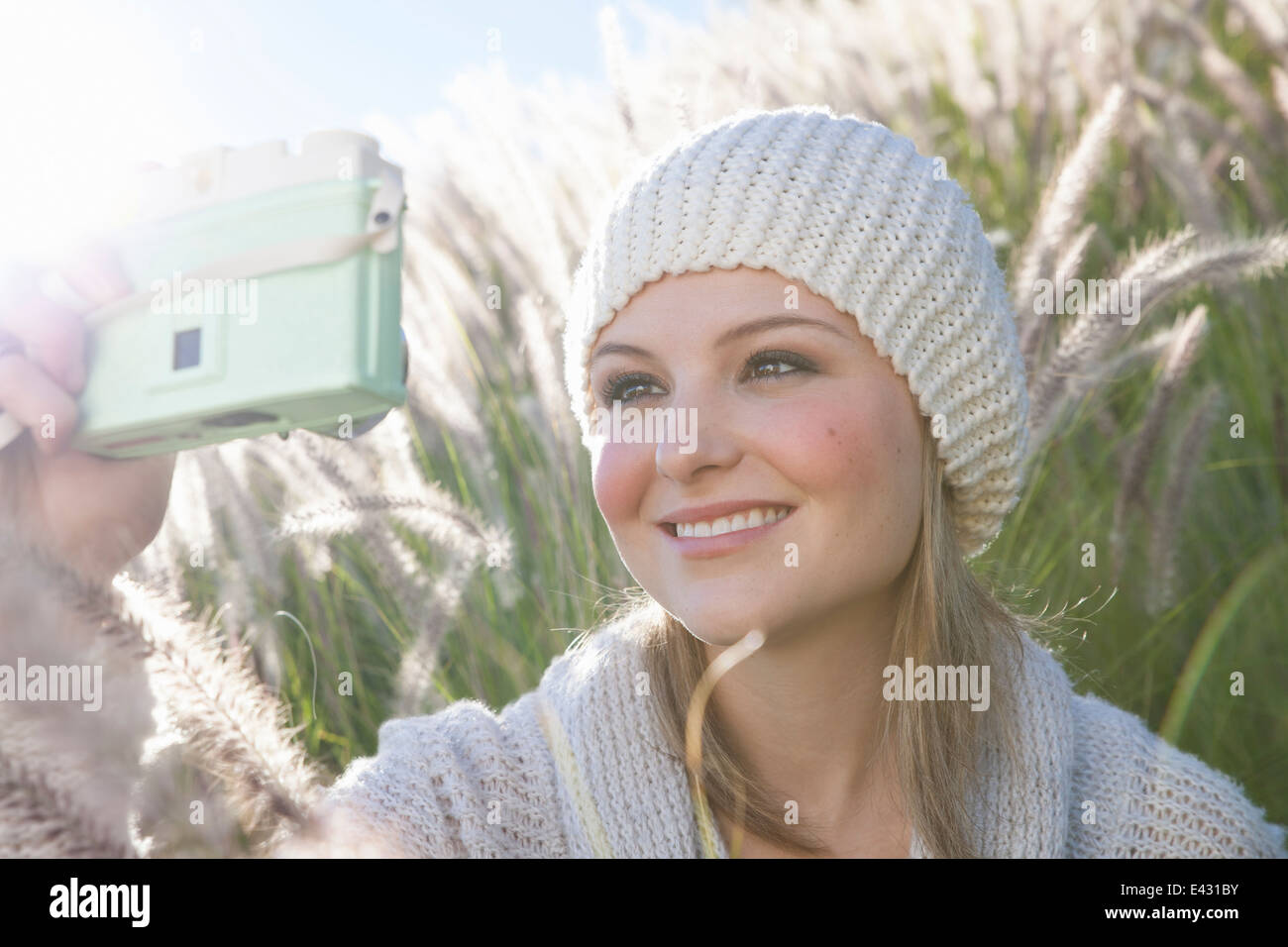 Jeune femme en tenant l'appareil photo numérique sur selfies dans l'herbe haute Banque D'Images