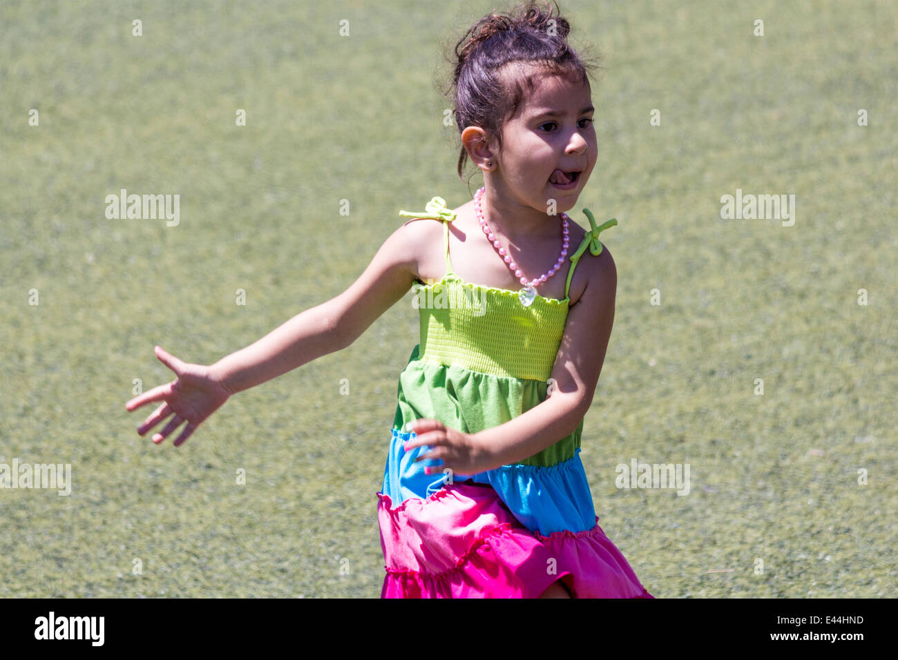 Petite fille danse sur l'herbe avec sa langue qui sort Banque D'Images
